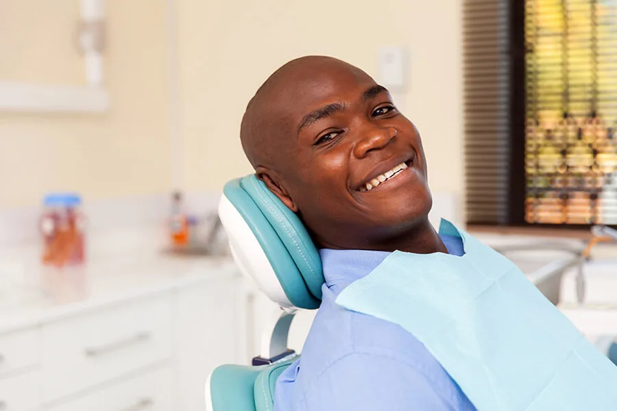 A smiling patient reclining in a dental chair wearing a dental bib.
